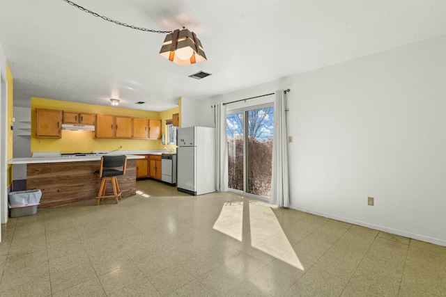 kitchen featuring visible vents, freestanding refrigerator, light countertops, under cabinet range hood, and brown cabinets