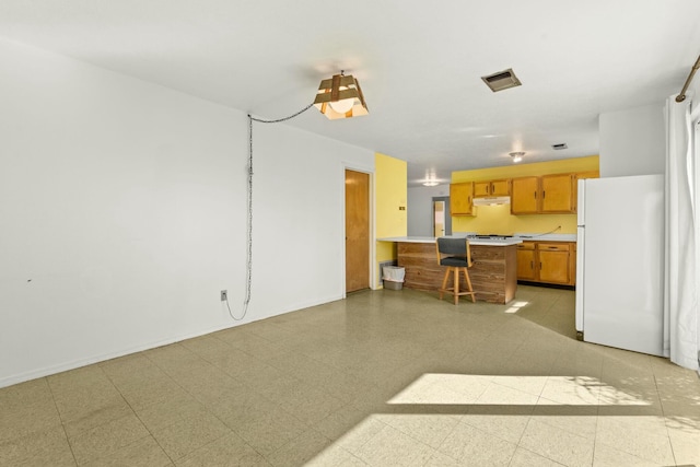 kitchen with visible vents, brown cabinets, freestanding refrigerator, a peninsula, and light countertops