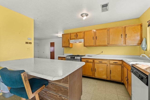 kitchen featuring visible vents, under cabinet range hood, a sink, a breakfast bar area, and white dishwasher