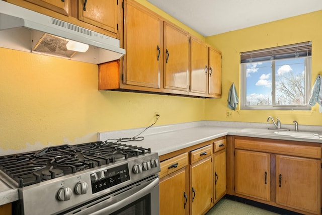 kitchen featuring stainless steel range with gas cooktop, under cabinet range hood, light countertops, brown cabinets, and a sink