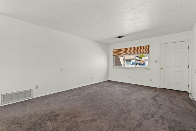 unfurnished room featuring visible vents, dark colored carpet, and a textured ceiling