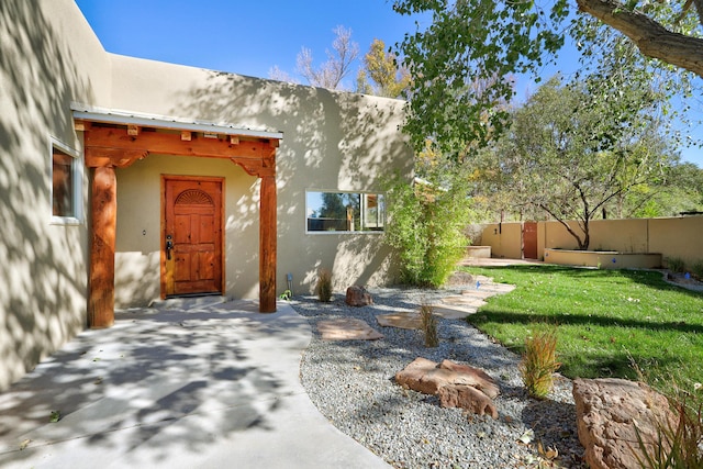 view of exterior entry with stucco siding, a yard, and fence