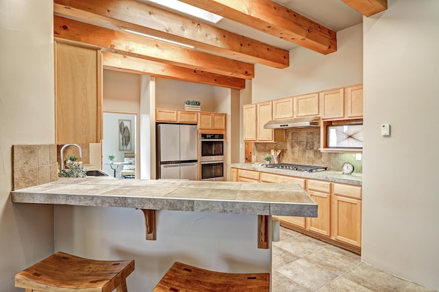 kitchen featuring a sink, under cabinet range hood, appliances with stainless steel finishes, and light brown cabinetry