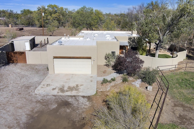 pueblo revival-style home with stucco siding, concrete driveway, and fence