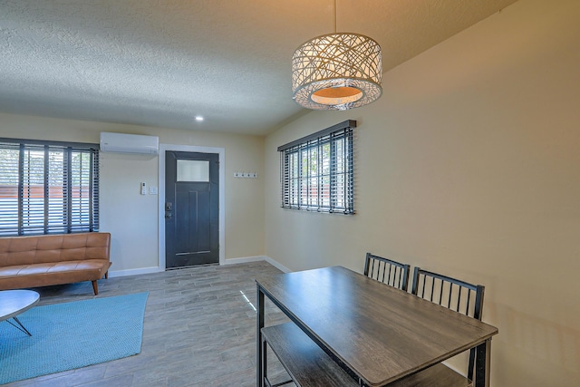 dining room featuring a textured ceiling, baseboards, a wall unit AC, and wood finished floors