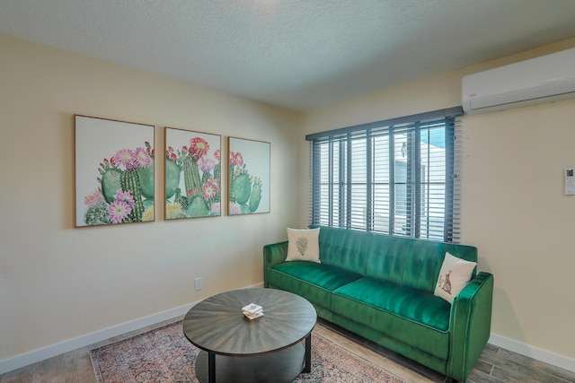 living area featuring a wall unit AC, wood finished floors, baseboards, and a textured ceiling