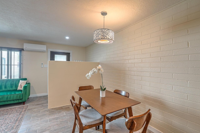 dining space with a textured ceiling, light wood-type flooring, brick wall, and a wall mounted AC