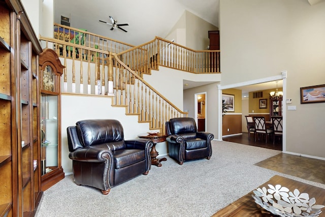 carpeted living room featuring stairway, ceiling fan with notable chandelier, baseboards, and a towering ceiling