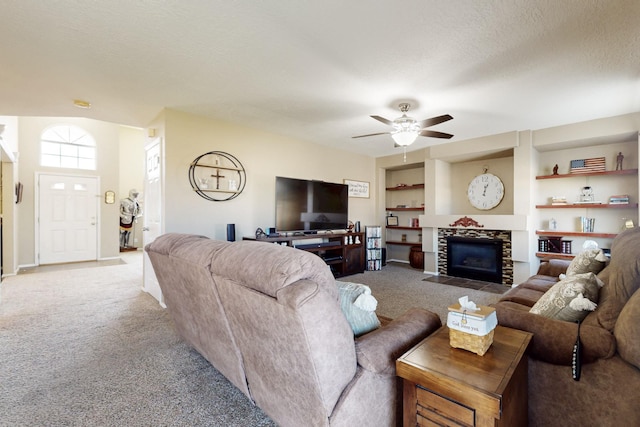 living area featuring a ceiling fan, carpet floors, a textured ceiling, and a tiled fireplace