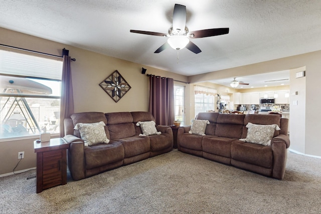 living area featuring light colored carpet, a textured ceiling, a ceiling fan, and baseboards