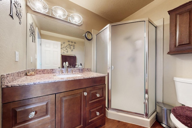 bathroom with vanity, wood finished floors, a shower stall, a textured ceiling, and toilet