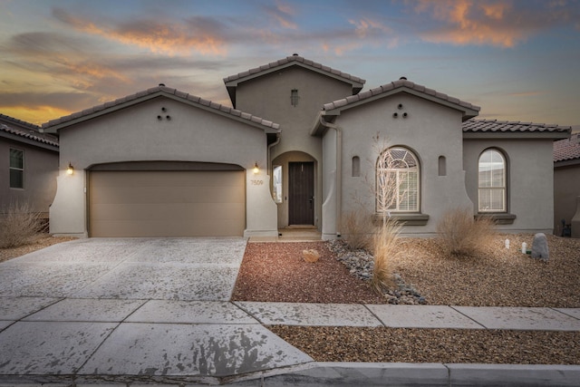 mediterranean / spanish-style house with stucco siding, a garage, concrete driveway, and a tiled roof