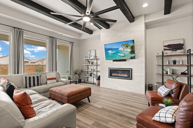 living room with a tiled fireplace, beamed ceiling, wood finished floors, and ceiling fan