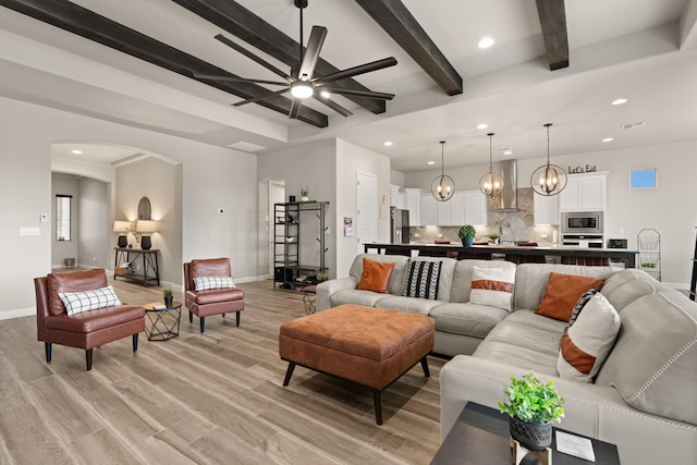 living room with beamed ceiling, arched walkways, light wood finished floors, baseboards, and ceiling fan