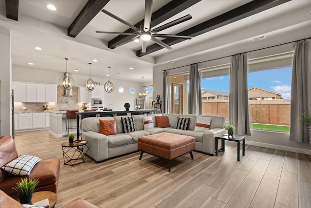 living room with beam ceiling, light wood-style flooring, a wealth of natural light, and ceiling fan with notable chandelier