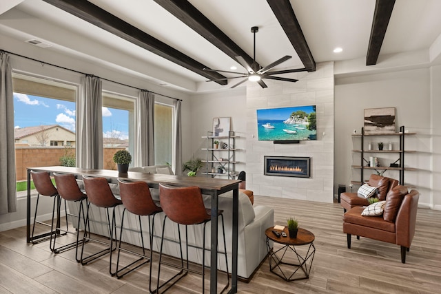 dining room with a tile fireplace, visible vents, beam ceiling, and wood finished floors