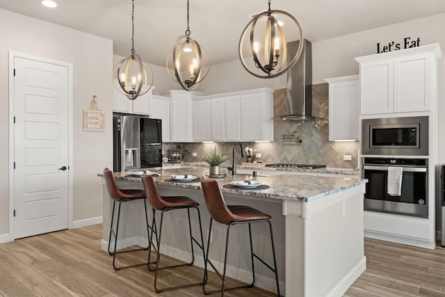 kitchen with wall chimney exhaust hood, an inviting chandelier, appliances with stainless steel finishes, and decorative backsplash