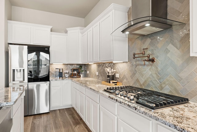 kitchen with wood finished floors, white cabinetry, stainless steel appliances, wall chimney range hood, and decorative backsplash