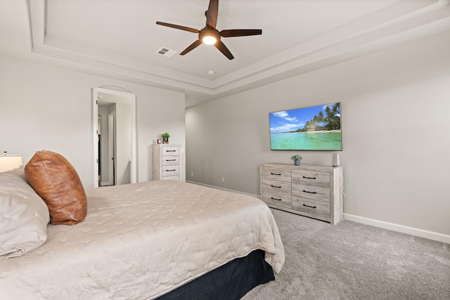 bedroom featuring visible vents, a raised ceiling, arched walkways, carpet, and baseboards