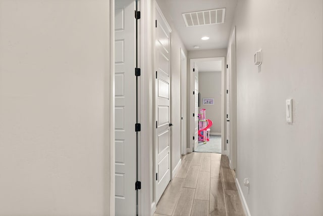 corridor featuring visible vents, baseboards, and wood finish floors