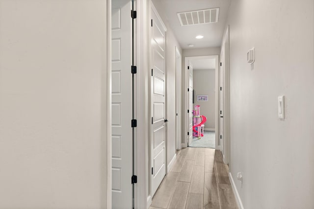 hallway featuring visible vents, wood finish floors, and baseboards