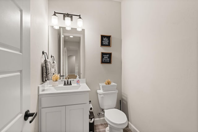 half bathroom featuring vanity, toilet, and baseboards