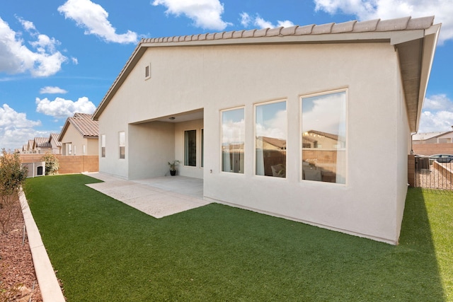 rear view of house with stucco siding, a yard, a fenced backyard, and a patio area