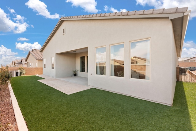 rear view of house featuring fence, stucco siding, a yard, and a patio area