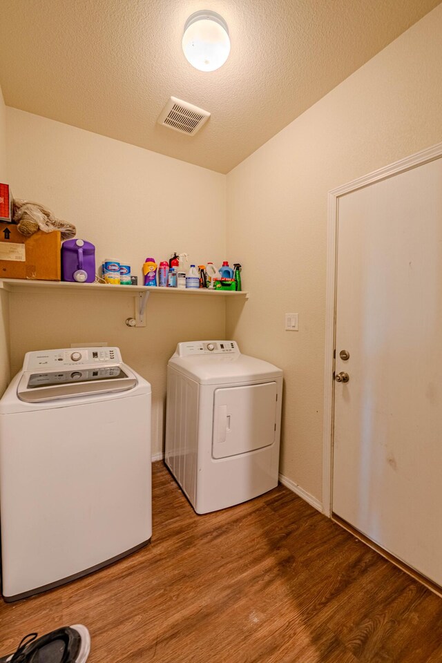 clothes washing area featuring visible vents, washer and clothes dryer, a textured ceiling, wood finished floors, and laundry area