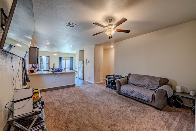 living room with visible vents, carpet flooring, a textured ceiling, and ceiling fan