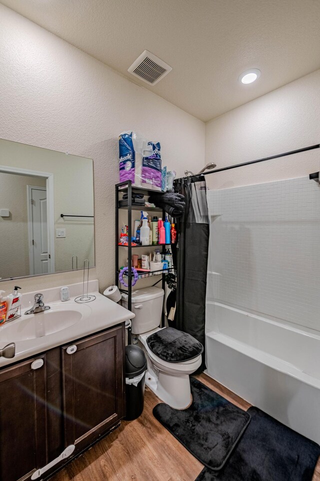 bathroom with visible vents, shower / bathtub combination with curtain, toilet, wood finished floors, and vanity