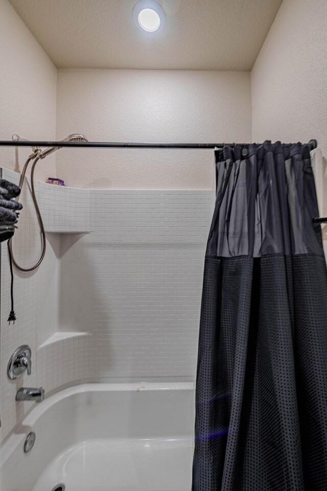 bathroom with shower / tub combo and a textured wall