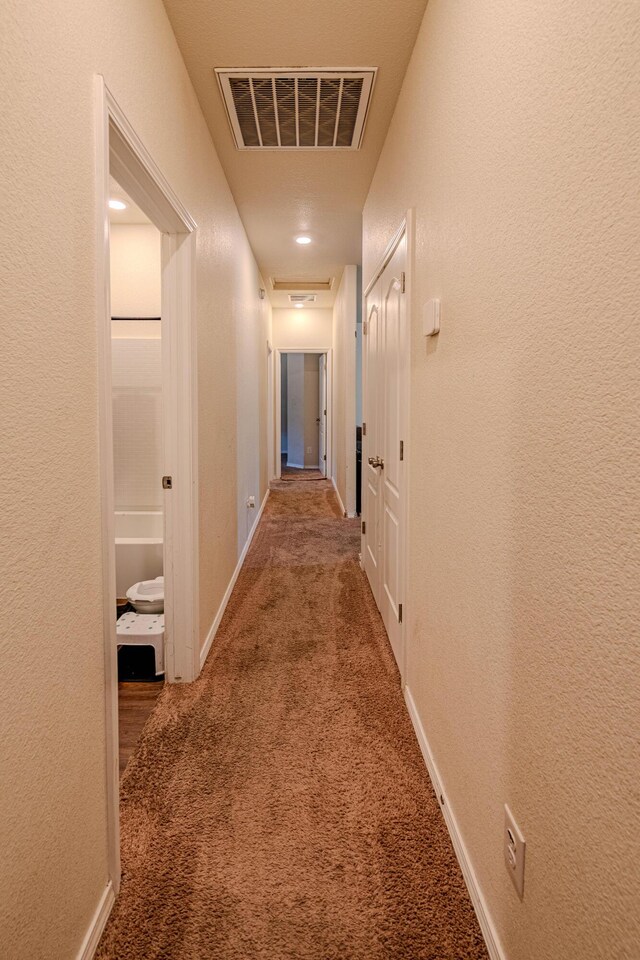 hallway with visible vents, carpet flooring, and a textured wall