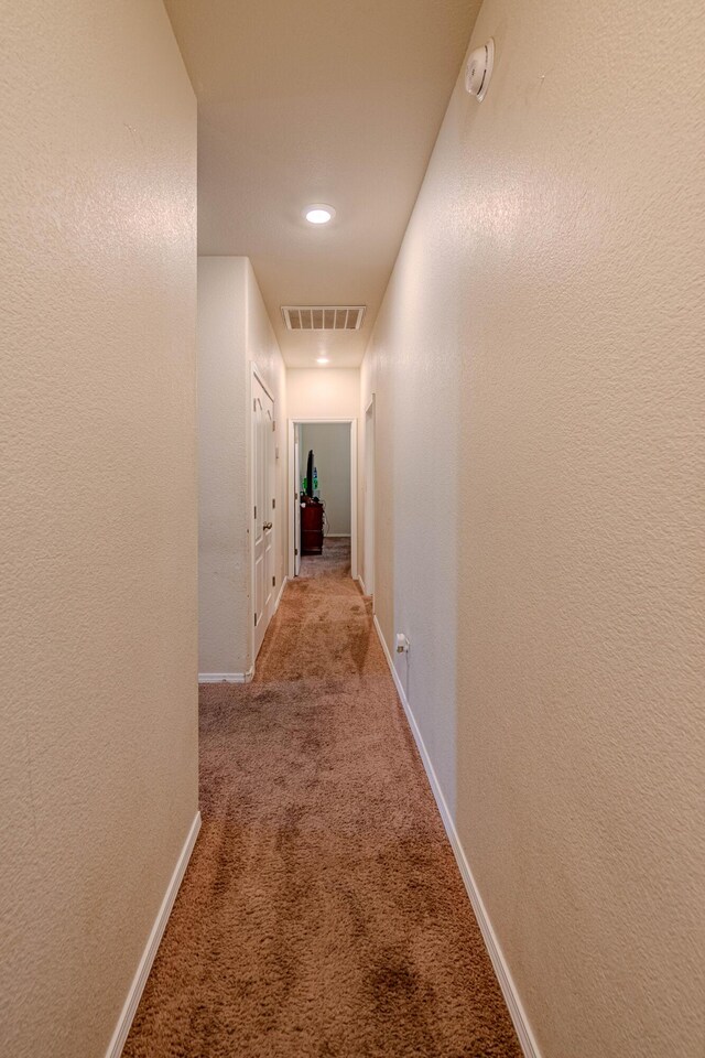 hallway featuring visible vents, baseboards, carpet, and a textured wall