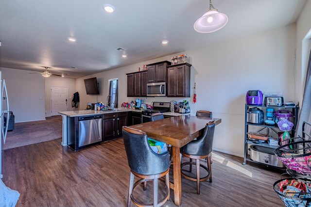 kitchen with dark wood finished floors, a peninsula, ceiling fan, dark brown cabinetry, and appliances with stainless steel finishes