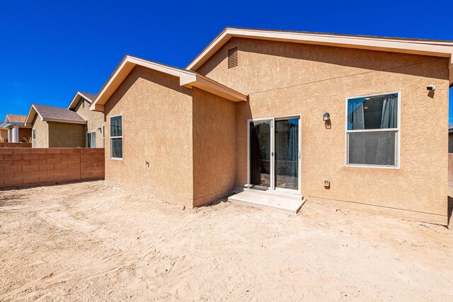 rear view of house with stucco siding and fence