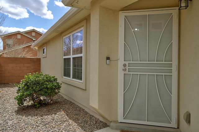 doorway to property with stucco siding and fence