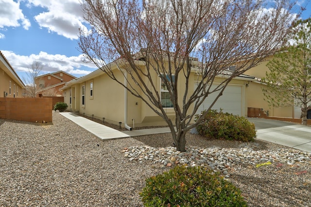 view of side of property featuring concrete driveway, an attached garage, fence, and stucco siding