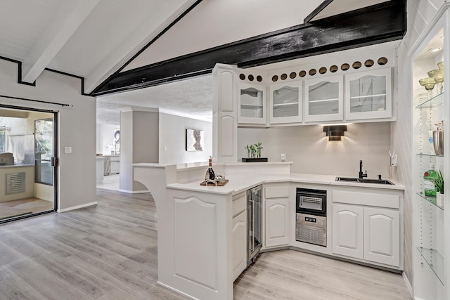 kitchen with light wood-type flooring, beverage cooler, a peninsula, light countertops, and glass insert cabinets