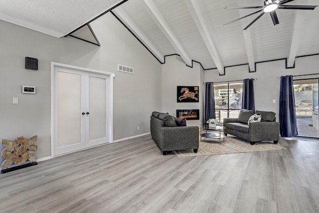 living room featuring a glass covered fireplace, beam ceiling, light wood-style flooring, and plenty of natural light