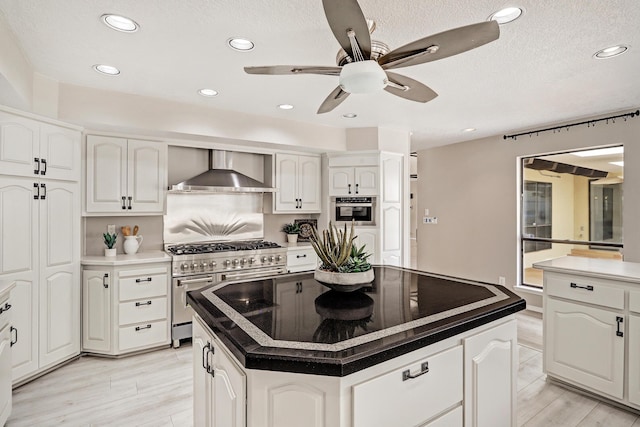 kitchen with white cabinets, wall chimney exhaust hood, appliances with stainless steel finishes, and a kitchen island