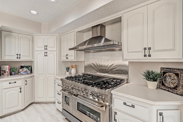 kitchen featuring double oven range, light wood-style flooring, light countertops, white cabinetry, and wall chimney exhaust hood