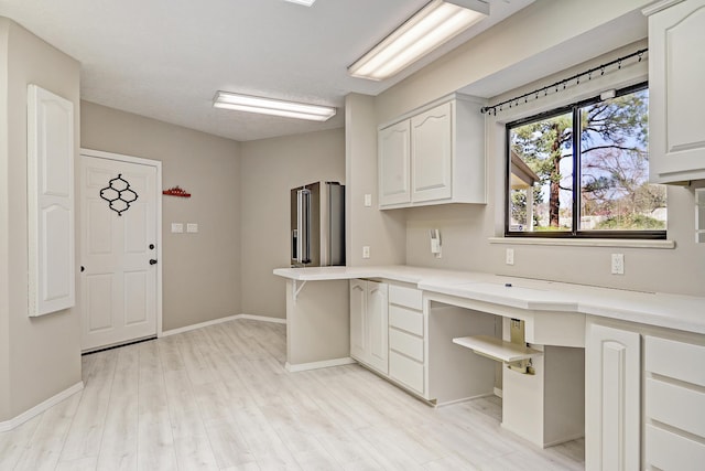 kitchen featuring light wood finished floors, baseboards, light countertops, built in desk, and white cabinetry