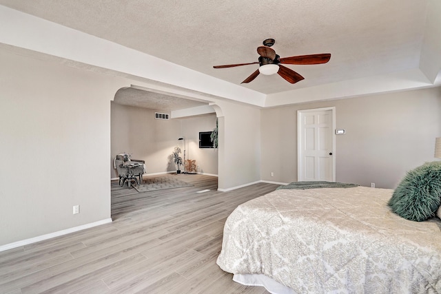 bedroom featuring arched walkways, a textured ceiling, baseboards, and wood finished floors