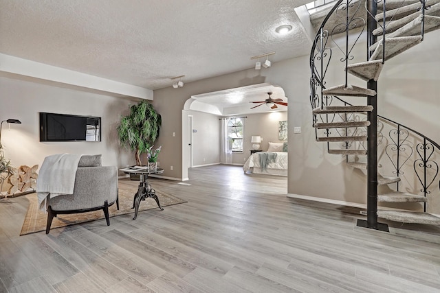 living area with arched walkways, stairway, a textured ceiling, and wood finished floors