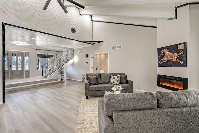 living room featuring visible vents, beamed ceiling, a glass covered fireplace, stairway, and baseboards