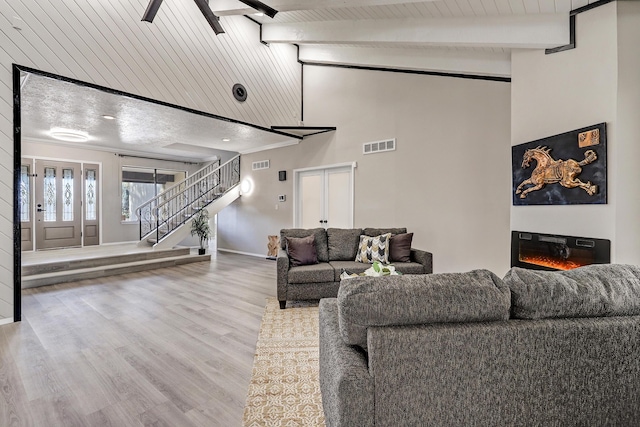 living area featuring visible vents, beam ceiling, wood finished floors, a glass covered fireplace, and stairway