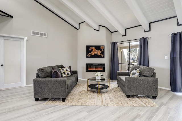 living room featuring visible vents, beam ceiling, a glass covered fireplace, and light wood-style flooring