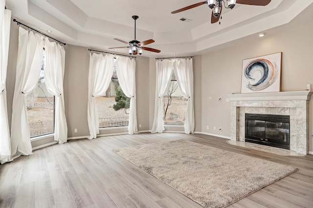 unfurnished living room featuring a tray ceiling, wood finished floors, a fireplace, and visible vents