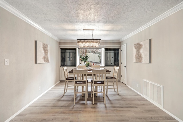 dining room with light wood-type flooring, visible vents, crown molding, baseboards, and a chandelier